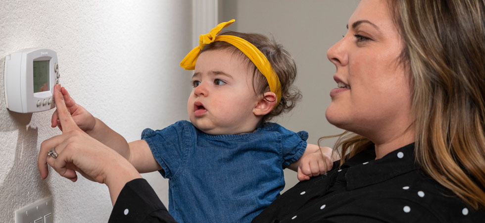 Mom holding daughter adjusting the thermostat on wall