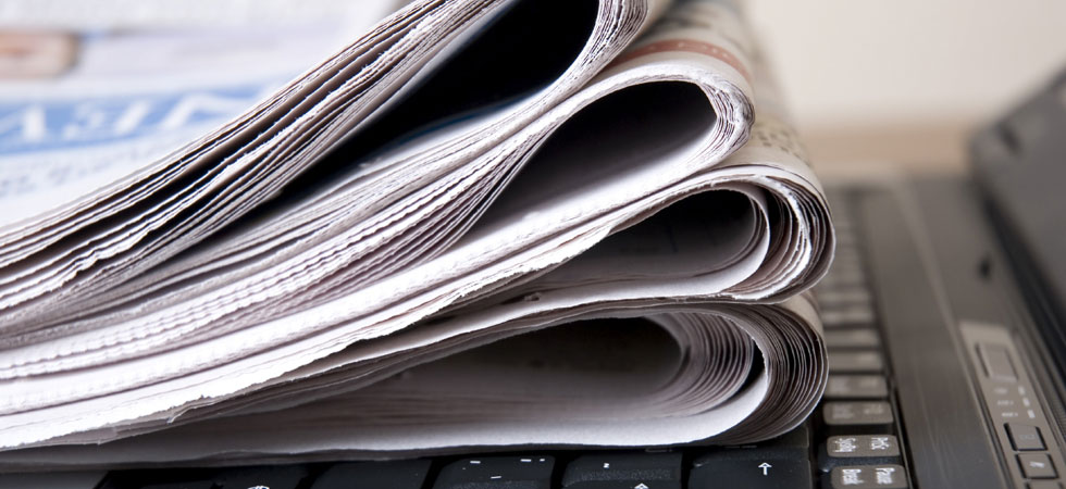 Stack of newspapers sitting on a laptop computer